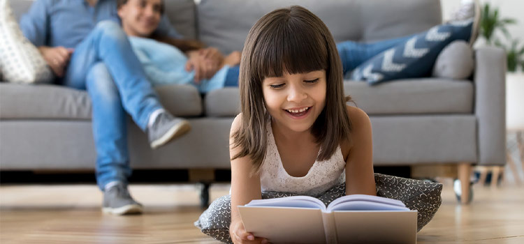 Une enfant qui lit un livre assise sur le carrelage