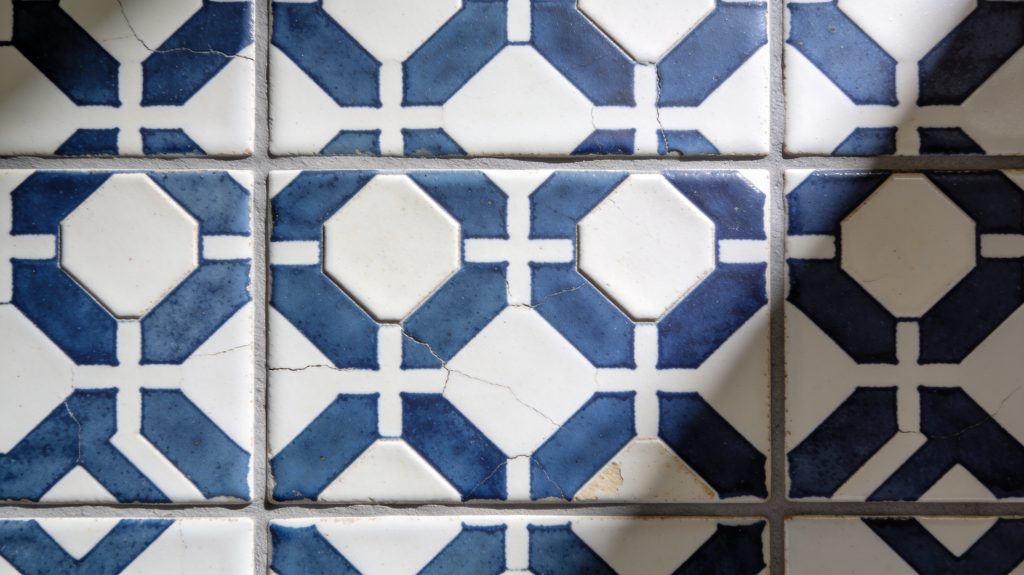 Gros plan sur des carreaux de ciment anciens blancs et bleus avec motifs géométriques et fissures apparentes.